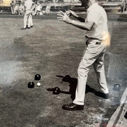 Black and white photo of a skp standing at the end of the green, watching a bowl come to a stop. 